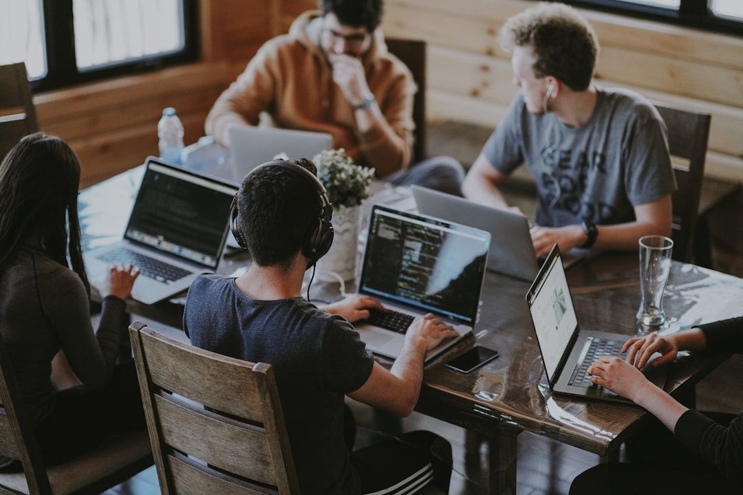 Team members collaborate around a table using laptops and headphones